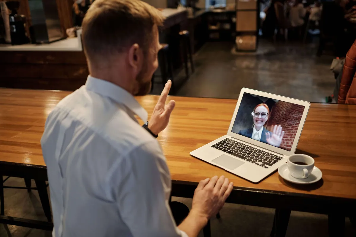 A first conversation: someone on a video call with a colleague, laptop open on a café table.
